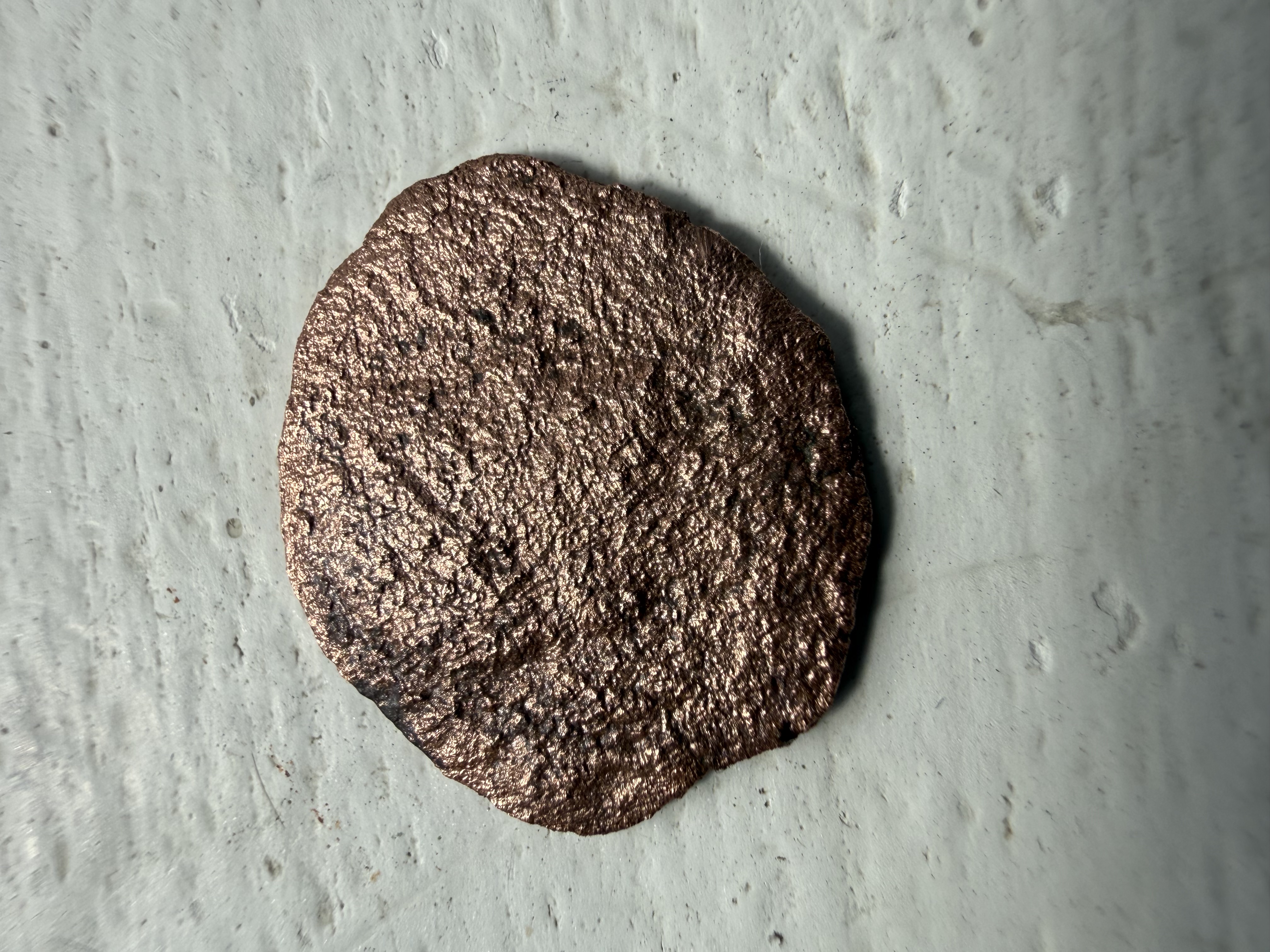 Cleaned copper-alloy disc with textured surface and rose-gold patination, found by metal detecting
