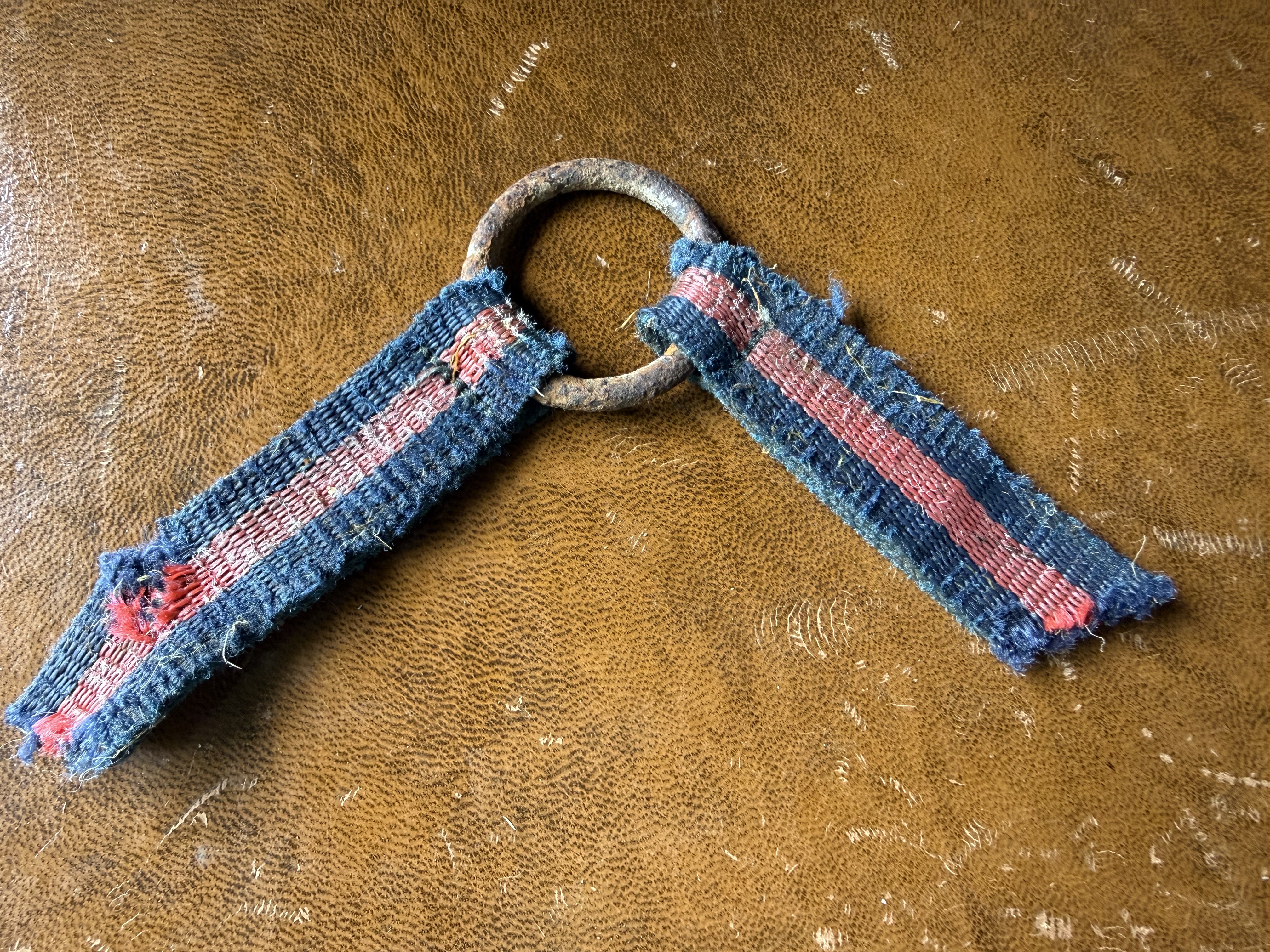 Fragment of blue and red woven textile strap threaded through a corroded iron ring, found by metal detecting